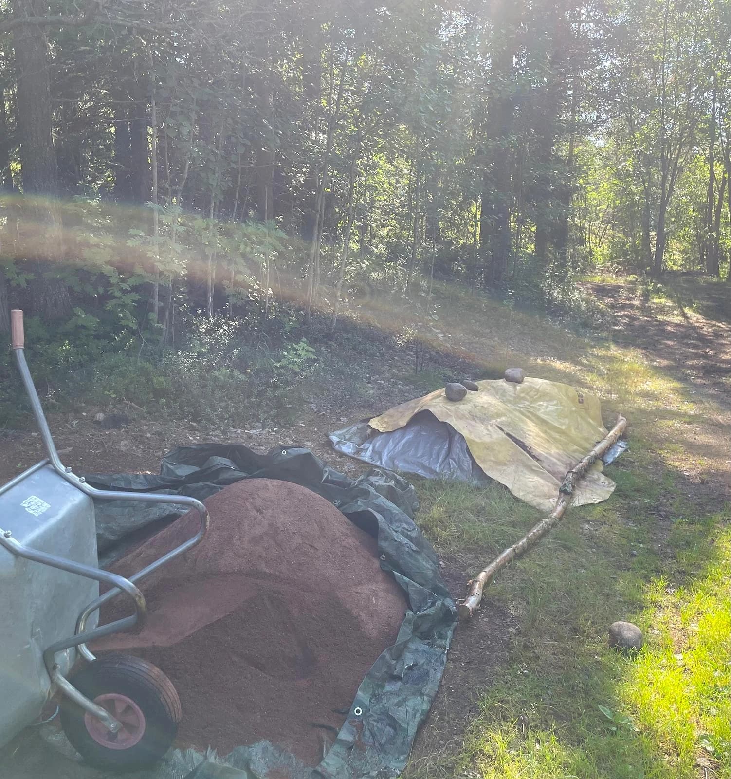 Siktat rött grus i högar under plast bredvid en skottkärra