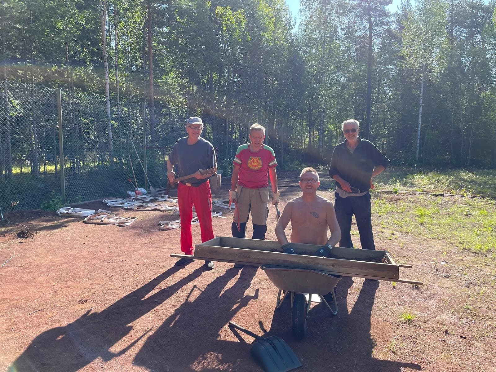 Fyra frivilliga på grusbanan med en skottkärra och en träsikt
