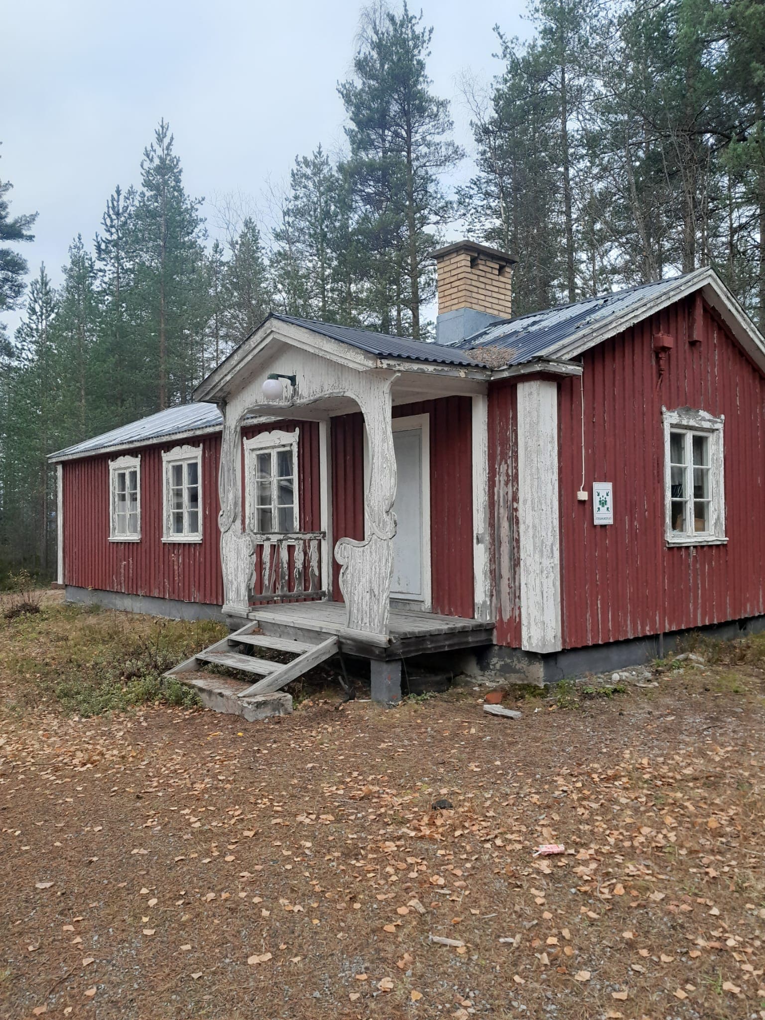 Red wooden cottage with a white porch and metal roof in a wooded setting